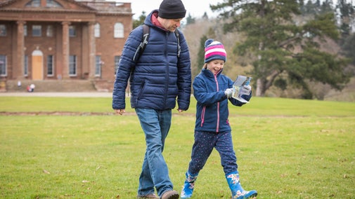 A man and a girl walking while looking at a map, dressed in winter clothes and wellies, with Berrington Hall in the background